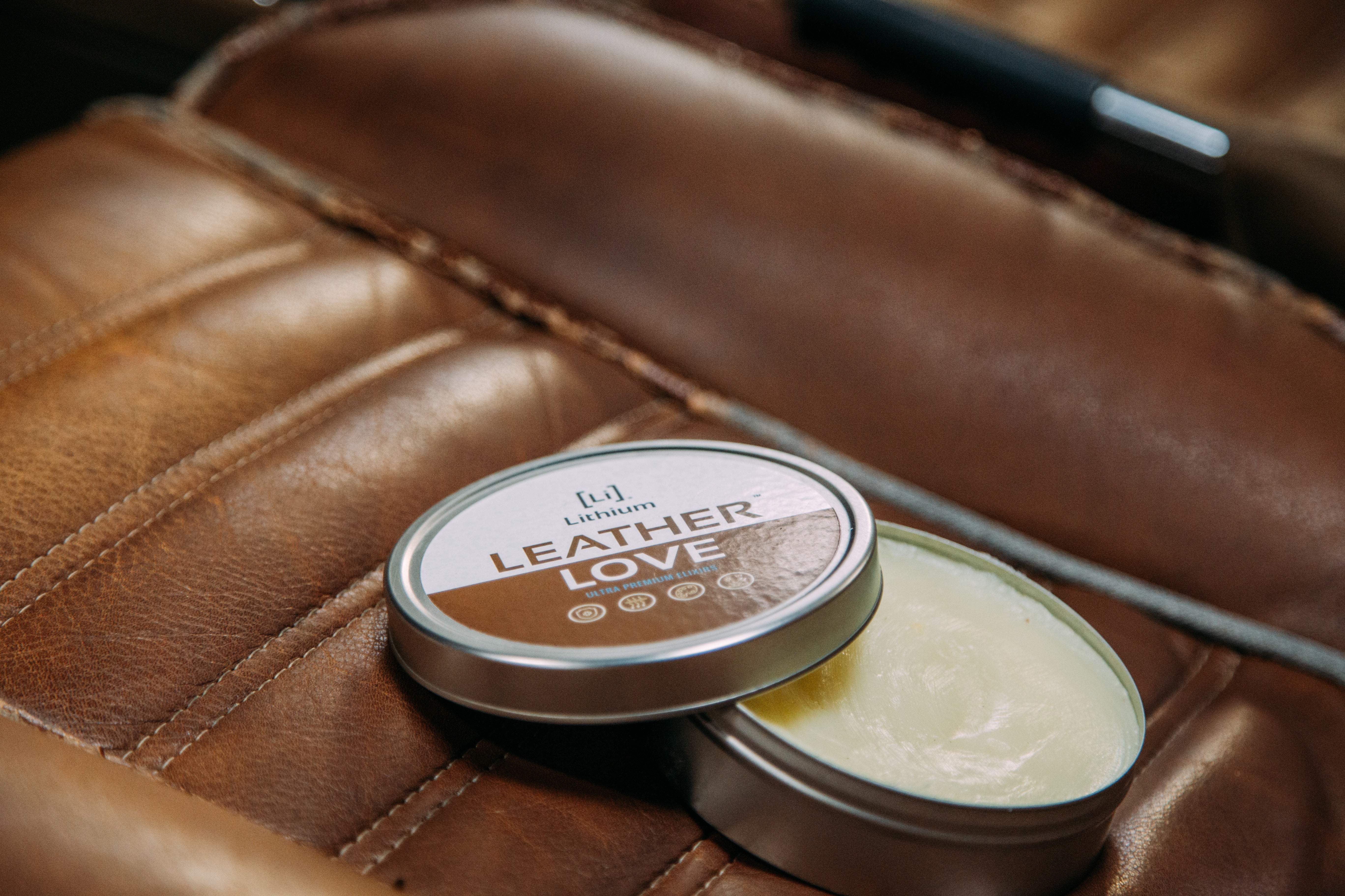 An open can of 'Leather Love' leather conditioner resting on rich, antique brown leather car seats, ready for application